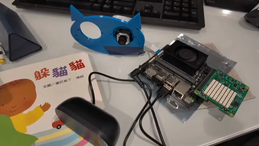 Hoot's prototype on a desk: a blue owl face with a camera, Jetson board, Sense HAT, speaker, and Chinese picture book.
